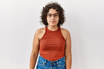Young hispanic woman wearing glasses standing over isolated background relaxed with serious expression on face. simple and natural looking at the camera.