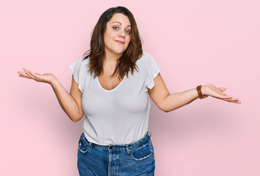 Young plus size woman wearing casual white t shirt clueless and confused expression with arms and hands raised. doubt concept.