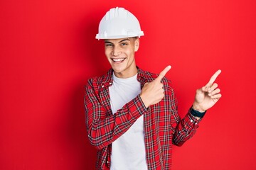 Young hispanic man wearing architect hardhat smiling and looking at the camera pointing with two...