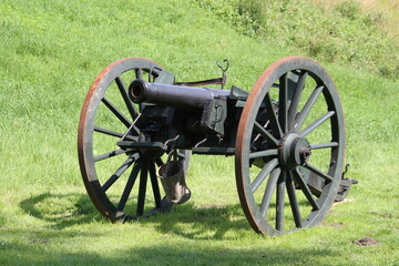 Historische  Kanone mit Speichenrädern auf der grünen Wiese - 453641137