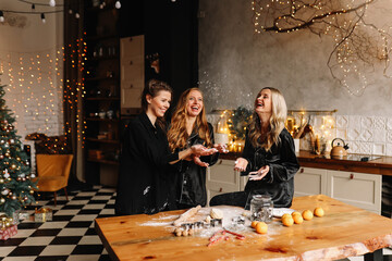 A group of cheerful female friends cook Christmas cookies, laugh, have fun and fool around in the kitchen in a cozy interior in the style of a loft house, selective focus