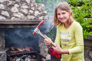 Children grilling meat. Happy teenage girl making barbecue on the grill on nature. Family camping...