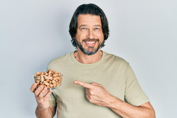 Middle age caucasian man holding peanuts smiling happy pointing with hand and finger
