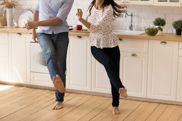 Focus on barefoot legs of happy young family couple dancing to music on warm wooden floor in modern...