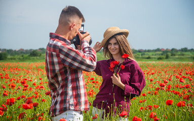couple in love of man and woman making photo on camera in summer poppy flower field, photographing
