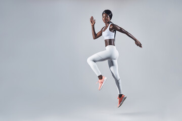 Fototapeta na wymiar Full length of confident young African woman in sports clothing jumping against gray background