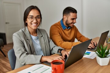 Two business workers smiling happy working sitting on desk at the office.