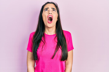 Young hispanic girl wearing casual pink t shirt angry and mad screaming frustrated and furious,...