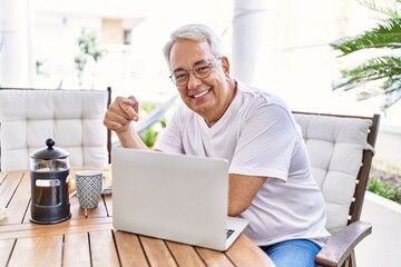 Handsome middle age hispanic man with grey hair and glasses working using computer laptop at home. Smiling happy and confident, relaxed at house terrace.