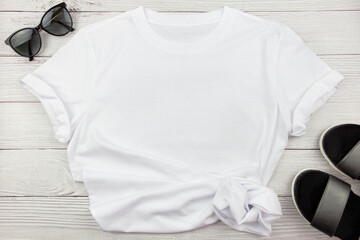 White womens cotton T Shirt mockup with summer shoes sandals and sunglasses on white wooden...