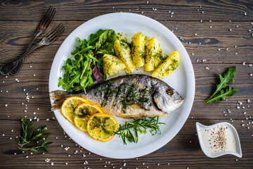 Roast sea bream  with potatoes and vegetables on wooden table
