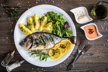 Roast sea bream  with potatoes and vegetables on wooden table
