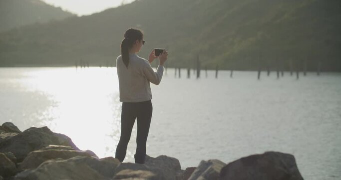 Woman use of mobile phone to take photo at seaside in the sunset time