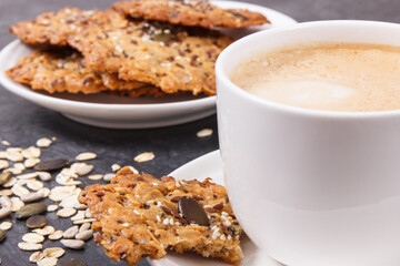 Cup of white coffee and fresh baked oatmeal cookies with honey and healthy seeds on plate. Delicious crunchy dessert