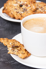 Cup of white coffee and fresh baked oatmeal cookies with honey and healthy seeds. Delicious crunchy dessert