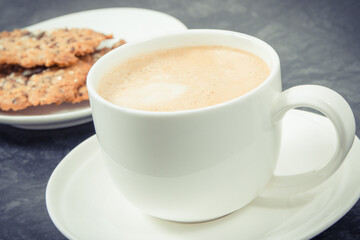 Cup of white coffee and fresh baked oatmeal cookies with honey and healthy seeds on plate. Delicious crunchy dessert