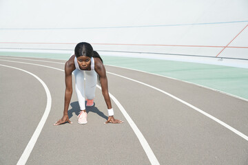 Concentrated young African woman standing at starting position on running track outdoors