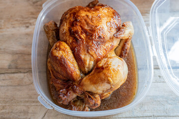Roast chicken with broth, in a plastic container on a wooden background. Take away food concept.