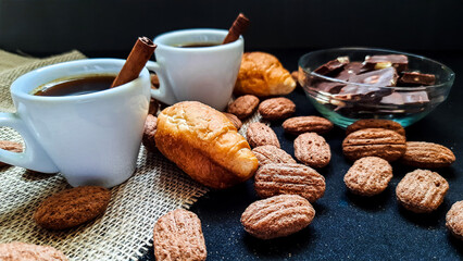 Two white coffee mugs with cinnamon and croissants on a dark background