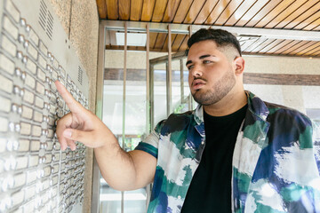 Fat latin man calling the intercom, with a serious expression. Latins and curvy models concept.