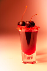 Ruby red cocktail based on vodka, cherry liqueur and syrup in drink shot glass, decorated with fresh cherry and red sugar