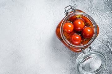 Pickled cherry tomatoes in a glass jar. White background. Top view. Copy space