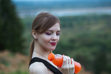 Woman wearing sportswear hydrating herself drinking vibrant orange juice during workout. Evening or...