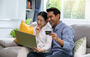 Pleasant family couple sitting looking at laptop screen. Happy young  spouse web surfing, making purchases online or booking flight tickets.