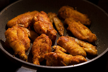 fried golden chicken wings in a pan on a black background