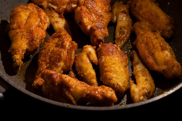 fried golden chicken wings in a pan on a black background