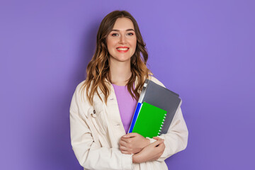 Caucasian student girl holding a book, notebook smiling, looking at the camera isolated on lilac...