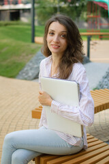 Female portrait of young woman with silver laptop, businesswoman is posing with digital tablet outside on modern building background, remote job