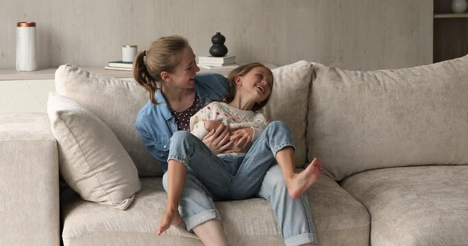 Cute little 8s girl sits on mothers laps, cheery family having fun enjoy playtime at home. Loving mom tickling laughing daughter. Happy motherhood, quarantine or weekend games with kids, bond concept