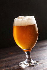 Glass goblet filled with fresh beer on table
