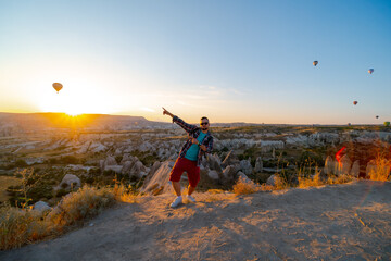 Happy man enjoy the sunrise. Tourist attraction balloon flight on background. Entertainment, tourism an vacation. Travel tour. Goreme, Cappadocia, Turkey.