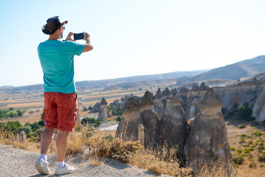 Male traveler takes picture, photo on smartphone, tourist Fairy chimneys park background (rock formations) Travel and vacation, tour Goreme, Cappadocia, Turkey.