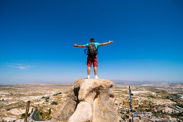 Back view. Man with arms spread apart enjoy the life. Uchisar Castle. Tourist at the top of the fortress, mountains, view of Cappadocia. Traveler at Destinaton. Turkey Vacation Summer day.