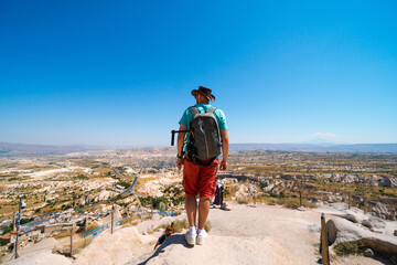 Fototapeta premium Uchisar Castle. Tourist at the top of the fortress, mountains, view of Cappadocia. Man photographer, male Traveler at Destinaton. Turkey Vacation and Tour Concept Summer day.