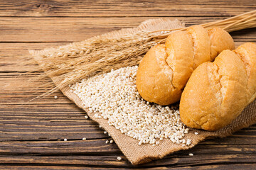 Bread with ears of wheat and wheat grains on a dark brown wooden table background In a rustic kitchen, top view.