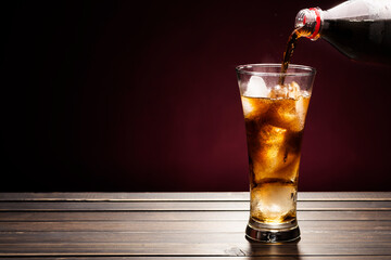 Pour sparkling water in a cola glass with ice cubes on a wooden table. on a dark black background.