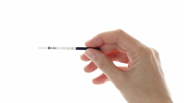 Caucasian female hand shows pregnancy test with two stripes against white background.