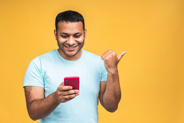 Portrait of handsome excited cheerful joyful indian african american guy wearing casual sending and getting messages to his lover isolated over yellow background. Using phone. Pointing finger.