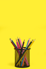 Office basket with colored pencils on yellow background.