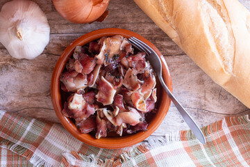 Fried pork ear, seasoned with garlic and parsley served in a clay pot, on a rustic wooden background, garnished with bread, garlic and onions. Typical Spanish tapa.