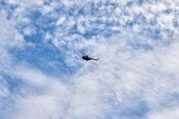 Flying helicopter against the background of a blue sky with spruce clouds