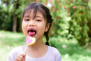 Portrait of toothless funny a little asian girl holding lollipops happily, eating sweets or lollipops will cause tooth decay. If you don't brush your teeth.