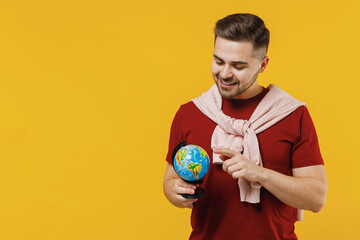 Smiling fun satisfied exploring cheerful happy young caucasian man 20s wear red t-shirt casual clothes hold in hands Earth world globe isolated on plain yellow color wall background studio portrait