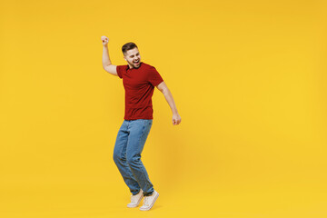 Fototapeta na wymiar Full length smiling happy caucasian young man 20s wear red t-shirt casual clothes stand on toes dancing have fun leaning back dancing isolated on plain yellow color wall background studio portrait