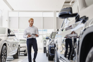 Full length smiling man customer male buyer client in white shirt read car papers documents choose...