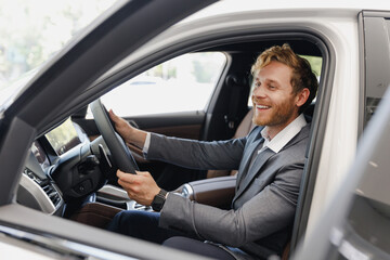 Satisfied man customer male buyer client wear classic grey suit driving car hold wheel choose auto want buy new automobile in showroom vehicle salon dealership store motor show indoor Sale concept